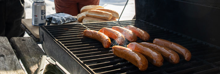 Early spring grill with sausages, people still wearing winter clothes, snow is on the ground