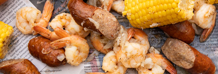 Low country boil with shrimp, Andouille sausage, corn, and potatoes spread across newspaper