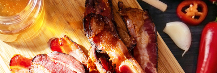 Sweet Heat Organic Applewood Smoked Uncured Bacon strips with a jar of honey, red chilis, and garlic