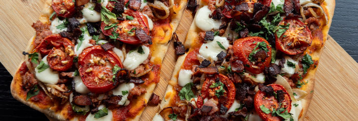 andouille and bacon flatbread with onion confit and melted fontina on a wooden board