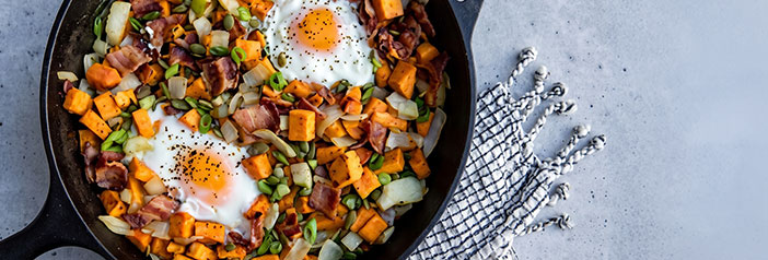 bacon and apple breakfast hash with a fried egg and runny yolk in a cast iron skillet