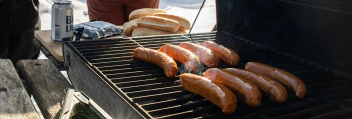 Early spring grill with sausages, people still wearing winter clothes, snow is on the ground